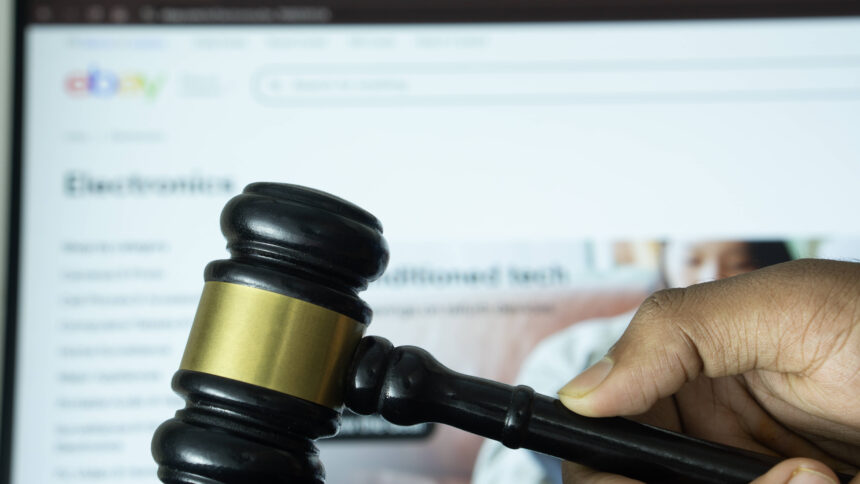 Eine Hand schlägt mit einem Richter*innenhammer auf einen Holzblock. Im Hintergrund ist die Webseite eines Online-Marktplatzes auf einem Latop.