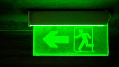 Ein grün beleuchtetes Schild, das auf einen Notausgang weist