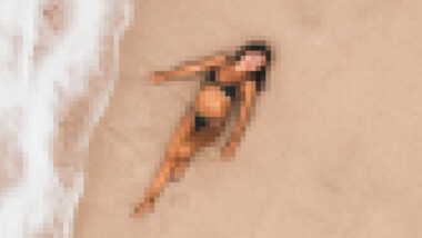 Frau im Bikini liegt am Strand. Bild ist verpixelt und sie nicht genau zu sehen