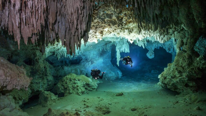 Zwei Höhlenraucher in einer mit sehr klarem Wasser gefüllten Tropfsteinhöhle.