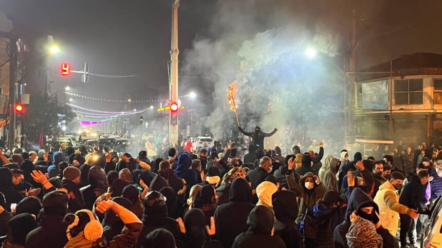 Menschen protestieren auf einer nächtlichen Straße. Ein Mann hält einen brennenden Gegenstand in der Hand.
