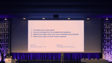 2 Vortragende und 1 Moderierender stehen vor einer großen Beamer-Leinwand