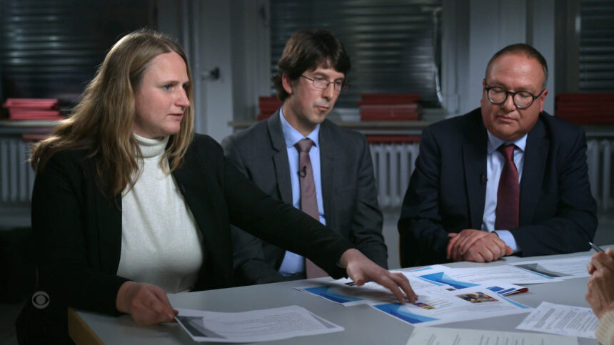 Zweii Männer und eine Frau sitzen an einem Tisch mit Akten.