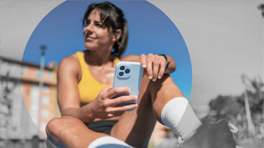 Eine Sportlerin rastet in der Sonne mit einem Smartphone in der Hand.