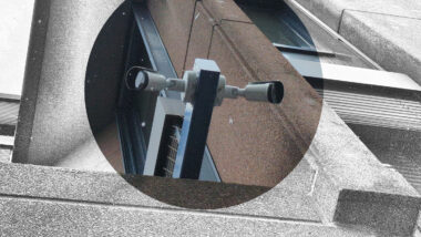 Zwei Kameras hängen an einem Mast an einer Fassade.