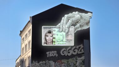 Hauswand ohne Fenster mit Graffiti, darauf eine Dürer-Hand, die einen Personalausweis hält