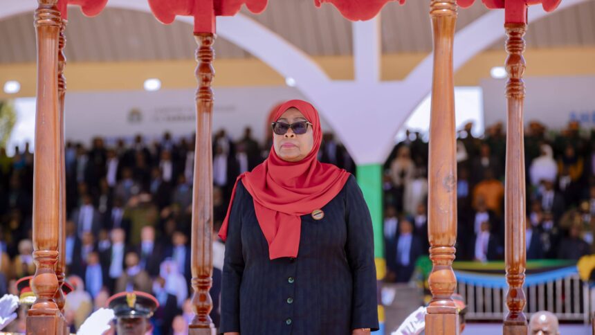 Eine streng blickende Frau mit rotem Kopftuch und Sonnenbrille, im Hintergrund Soldaten