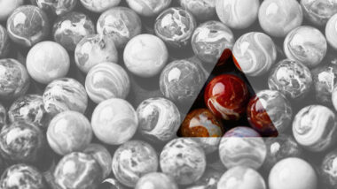 Ein Bild von Murmeln, der Großteil in Graustufen, nur ein dreieckiger Ausschnitt zeigt rot gefärbte Murmeln