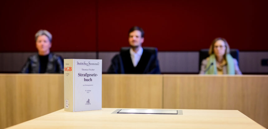 Verschwommenes Foto von zwei Schöff:innen und einem Richter, im Vordergrund ein Strafgesetzbuch