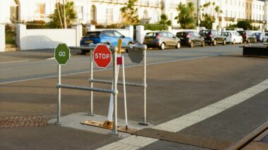 Eine Straße im Sonnenlicht, im Vordergrund Verkehrsschilder auf den "Stop" in rot und "Go" in grün stehen