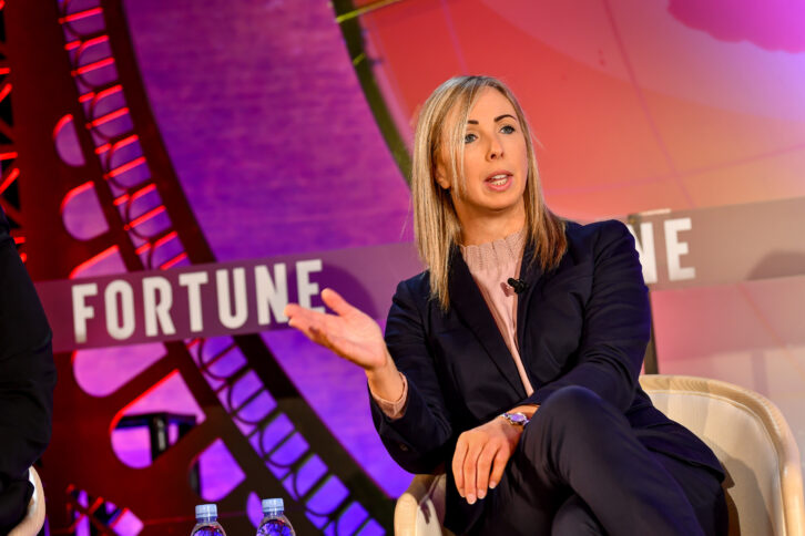 Eine weiße Frau mittleren Alters im schicken Anzug spricht auf einem Podium.