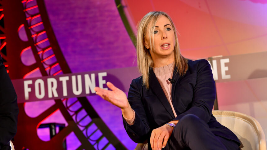Eine weiße Frau mittleren Alters im schicken Anzug spricht auf einem Podium.