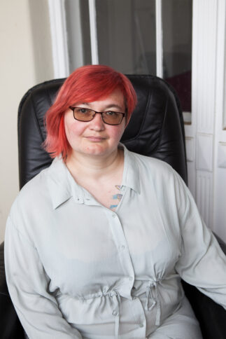 Eine Person mit roten mittellangen roten Haaren sitzt in einem schwarzen Bürostuhl.