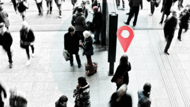 Menschengewusel an einem Bahnhof, in der Mitte eine Person mit einem Ortsmarker über dem Kopf