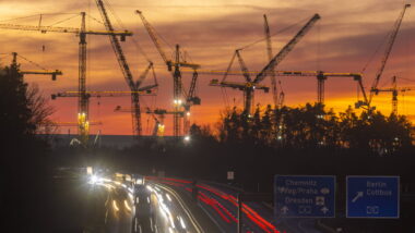 Baukräne im Abendlicht von einer Autobahn aus gesehen.