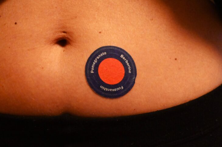 Auf einem Bauch klebt ein rundes rotes Pflaster mit schwarzem Rand.