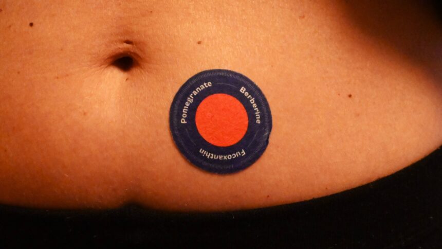 Auf einem Bauch klebt ein rundes rotes Pflaster mit schwarzem Rand.