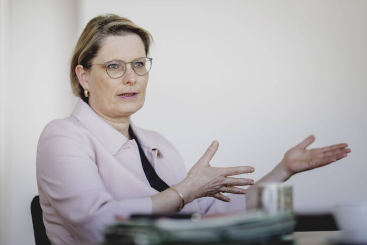 Person in rosa Blazer und mit Brille sitzt und gestikuliert in einem Gespräch