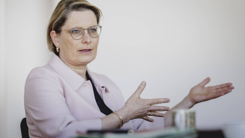 Person in rosa Blazer und mit Brille sitzt und gestikuliert in einem Gespräch