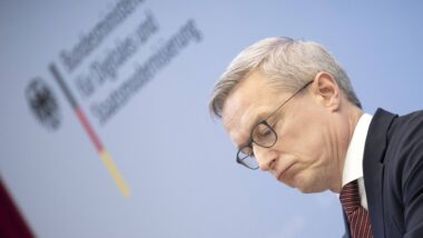 Ein Gesicht im Profil, im Hintergrund eine graue Wand mit dem Logo des Digitalministeriums