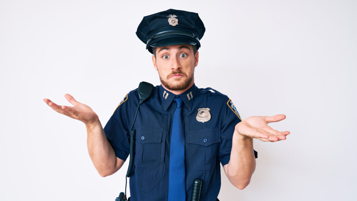 Ein junger weißer Mann in Polizeiuniform mit ratlosem und verwirrtem Gesichtsausdruck, der Arme und Hände hochgestreckt hat.