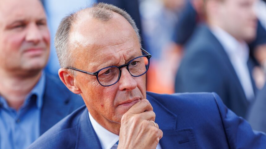 Mann mit Anzug, Halbglatze und Brille hält seine Hand in Denkerpose vor den Mund.