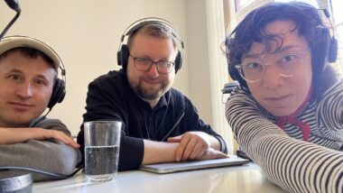 Drei Personen mit Kopfhörer machen Selfie am Tisch