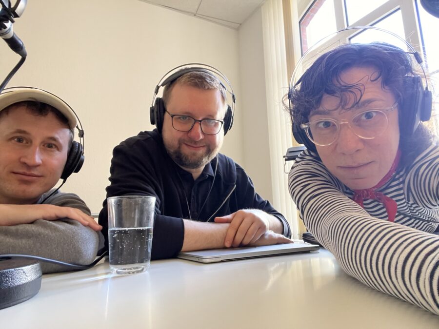 Drei Personen mit Kopfhörer machen Selfie am Tisch