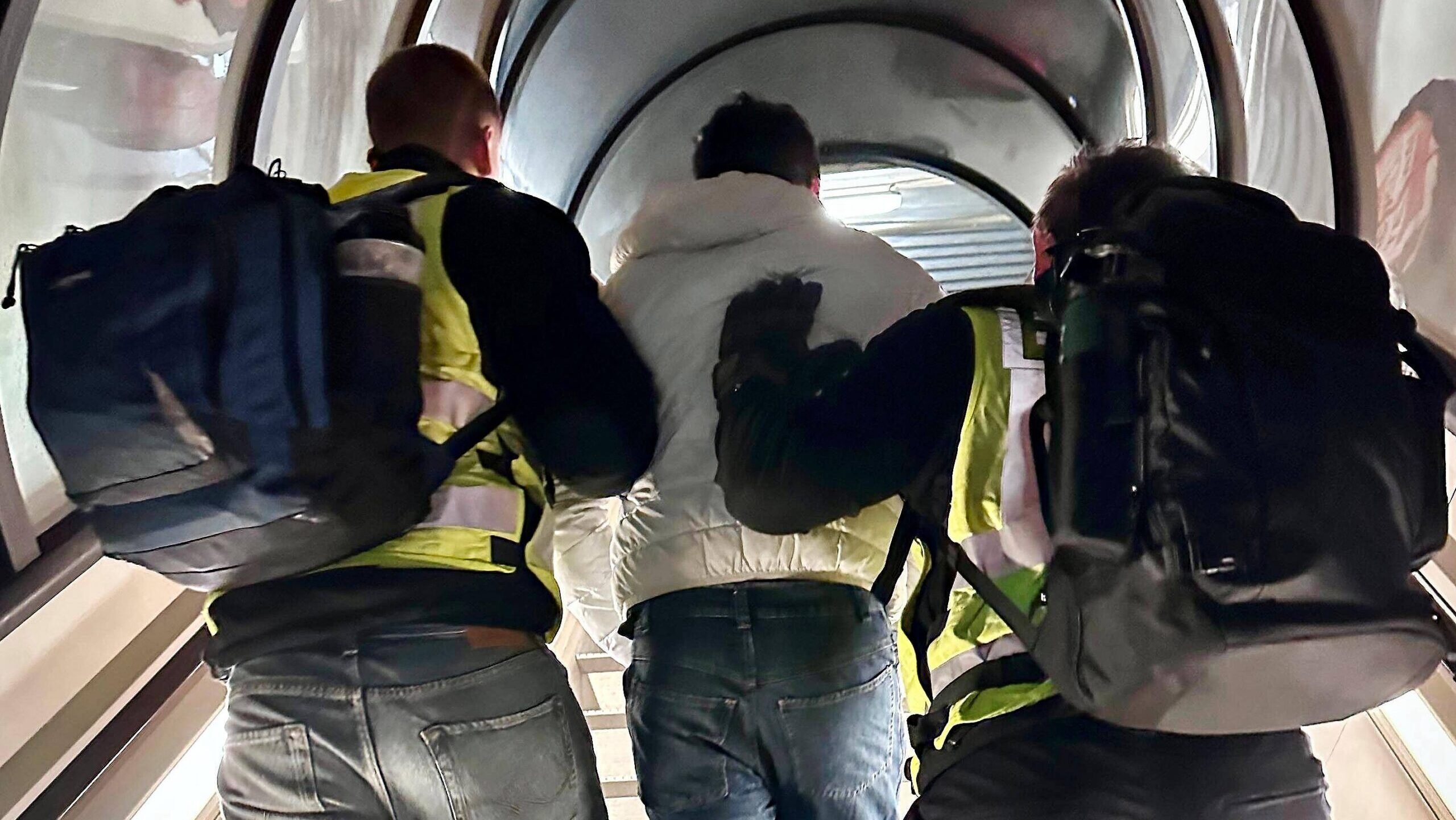 Zwei Polizisten bringen eine Person durch eine Gangway in ein Flugzeug.