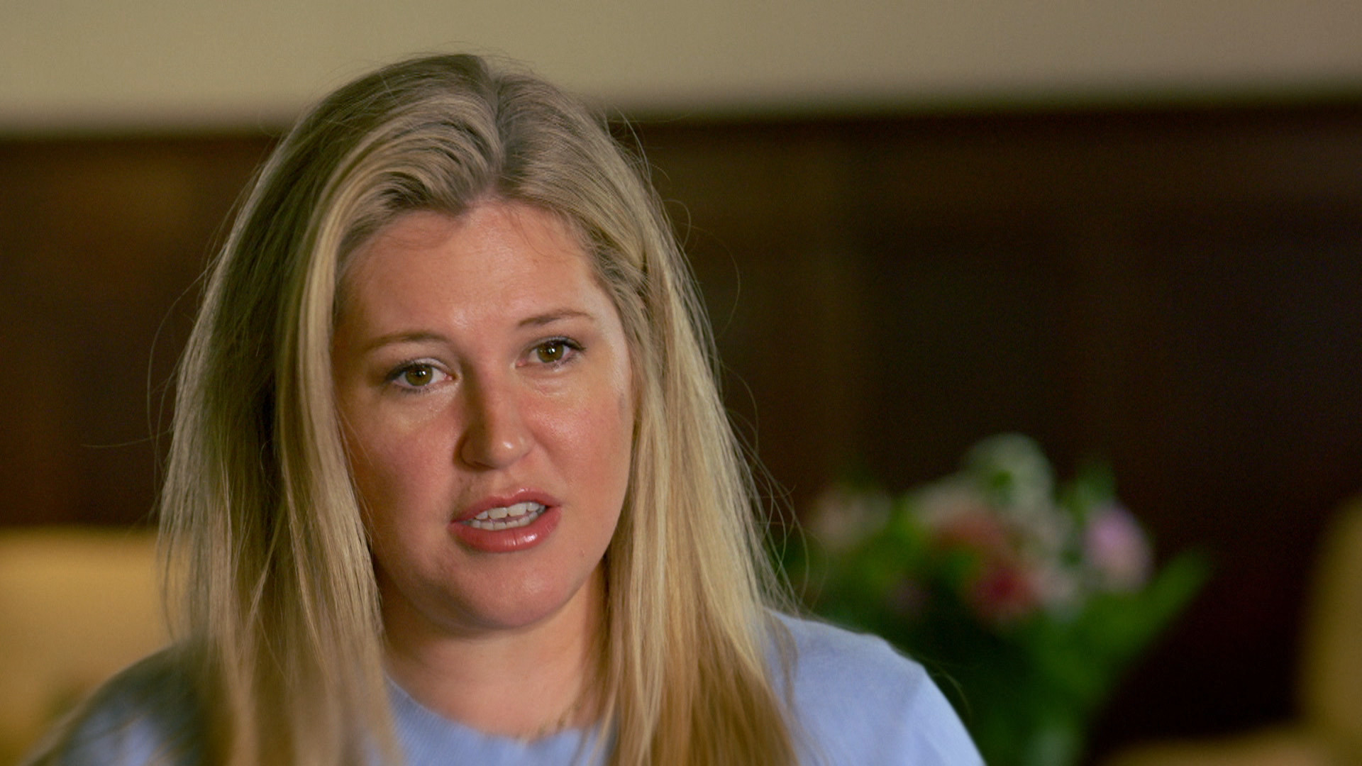 Eine Frau mit langen, blonden Haaren; im Hintergrund ein Blumenstrauß.