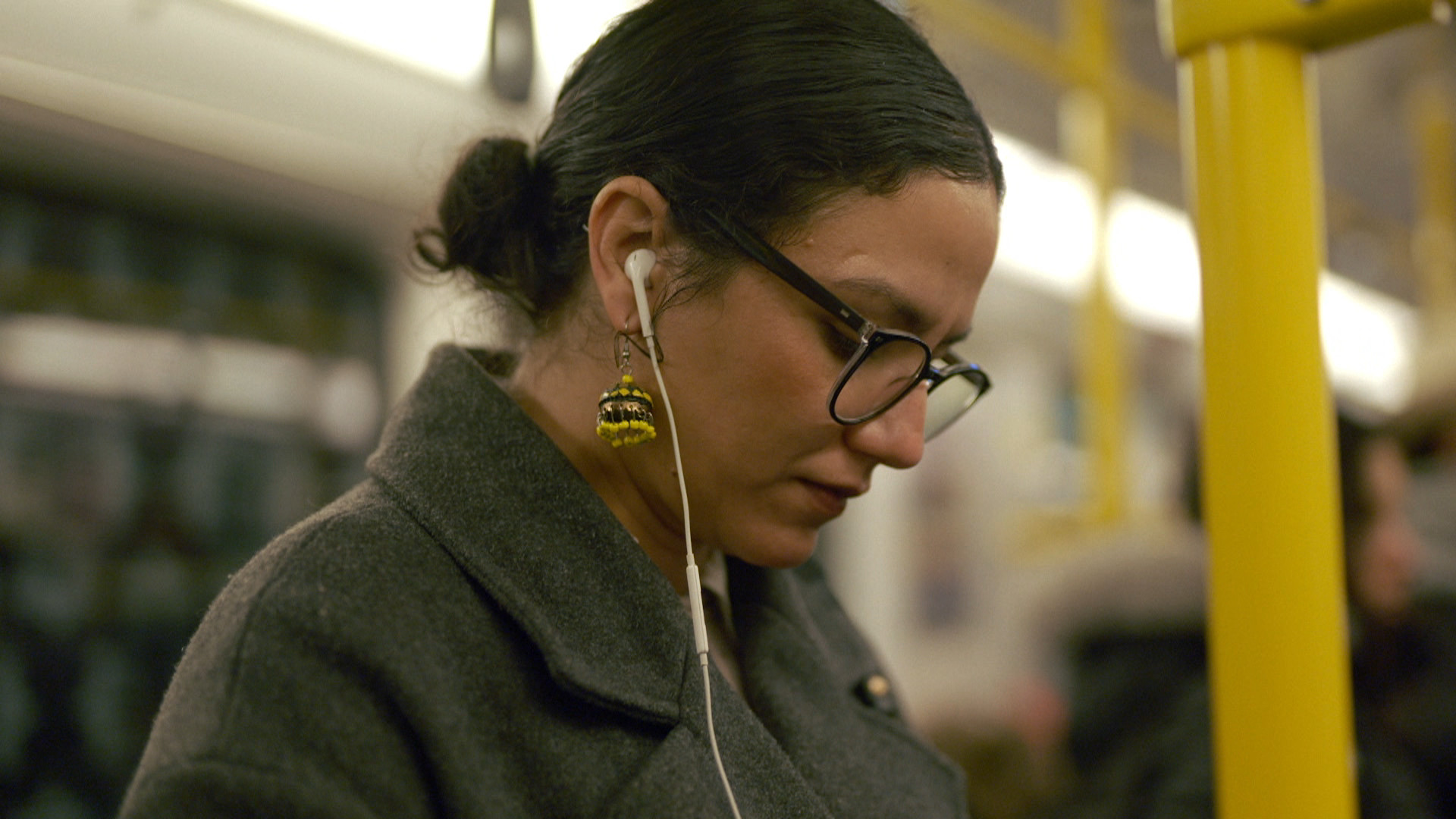 Eine Frau in der U-Bahn mit Brille und In-Ear-Kopfhörern.