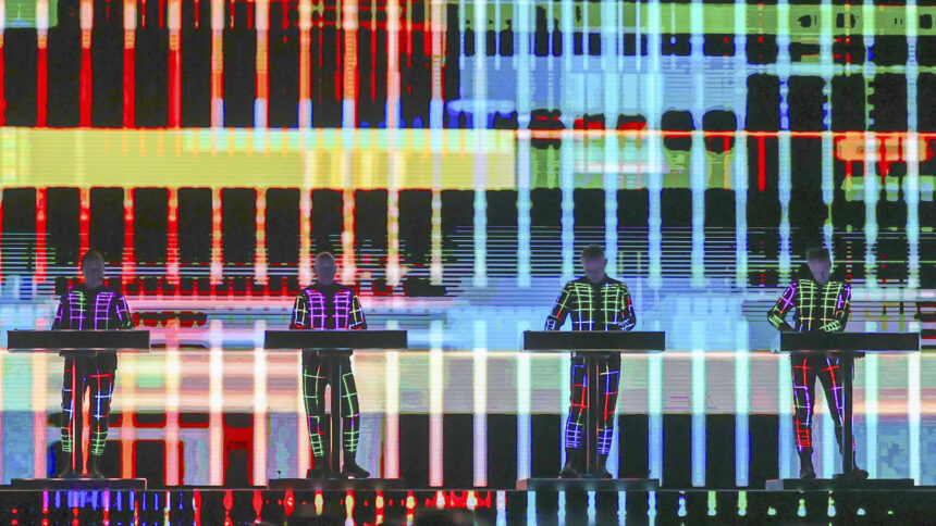 Vier Musiker stehen hinter elektronischen Instrumenten vor einer großen, farbigen, geometrischen Lichtprojektion