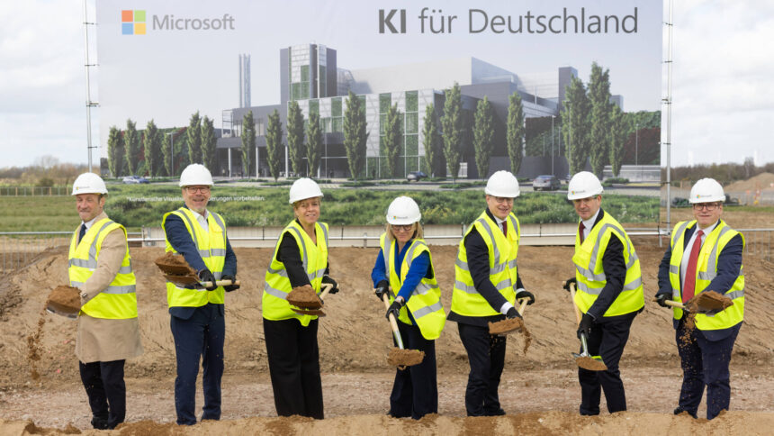 Sieben nahezu identifisch aussehende Menschen in Anzügen, gelbden Warnwestern und Baustellen-Helmen stehen mit Spaten auf einer Baustelle. Im Hintergrund ein großes Werbeplakat mit einem grün und modern wirkenden Gebäude, Schriftzug: "Microsoft - KI für Deutschland"