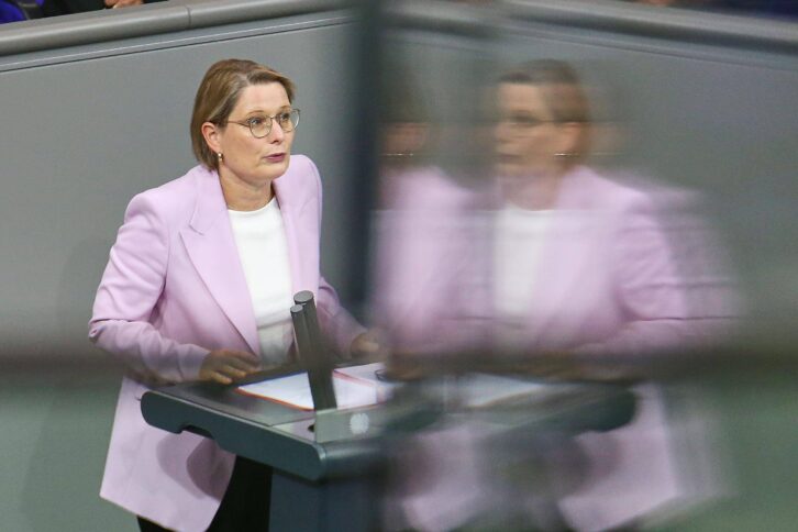 Person im lila Blazer steht an Rednerpult im Bundestag