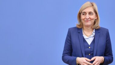 Ministerin Nina Warken mit Merkel-Raute vor einer blauen Wand.