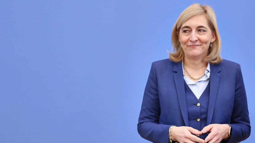 Ministerin Nina Warken mit Merkel-Raute vor einer blauen Wand.