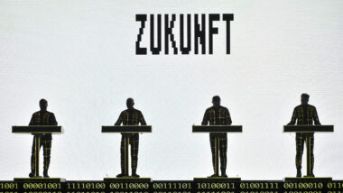 Die Band Kraftwerk steht vor einem weißen Bildschirm, auf dem ZUKUNFT steht
