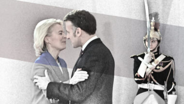 Emmanuel Macron begrüßt Ursula von der Leyen mit einem angedeuteten Kuss. Im Hintergrund steht eine bewaffneter Gardist.