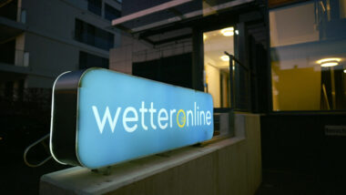 Ein Gebäude im Dunkeln, im Vordergrund ist ein großes beleuchtetes Schild mit der Aufschrift "WetterOnline" zu sehen, weiße Schrift auf blauem Grund