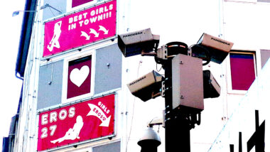 Eine Kamera vor einer Fassade an der Werbung für Bordelle hängt.