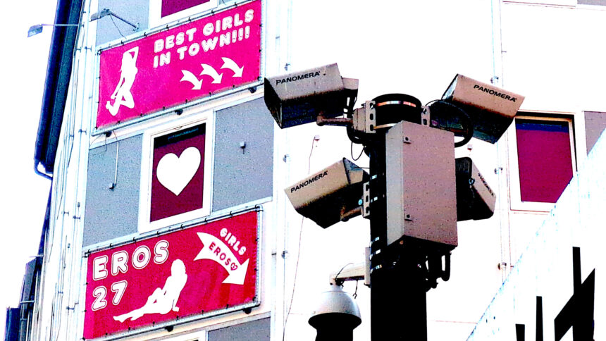 Eine Kamera vor einer Fassade an der Werbung für Bordelle hängt.