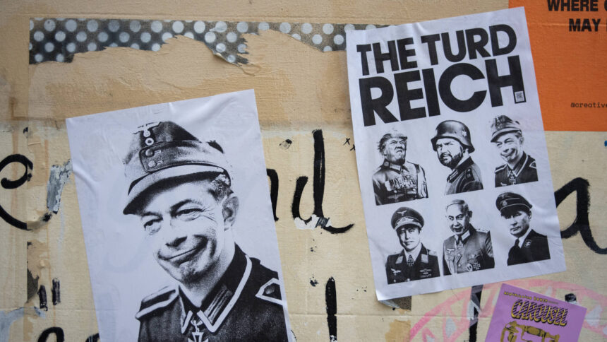 Wand mit verschiedenen aufgeklebten Postern und Graffiti. Im Vordergrund links ist ein Schwarz-Weiß-Porträt von Elon Musk in Militäruniform mit einem Grinsen zu sehen. Daneben rechts befindet sich ein weiteres Poster mit der Überschrift "THE TURD REICH", darunter sind mehrere Porträts von Männern in ähnlichen Uniformen abgebildet, unter anderem Trump und JD Vance.