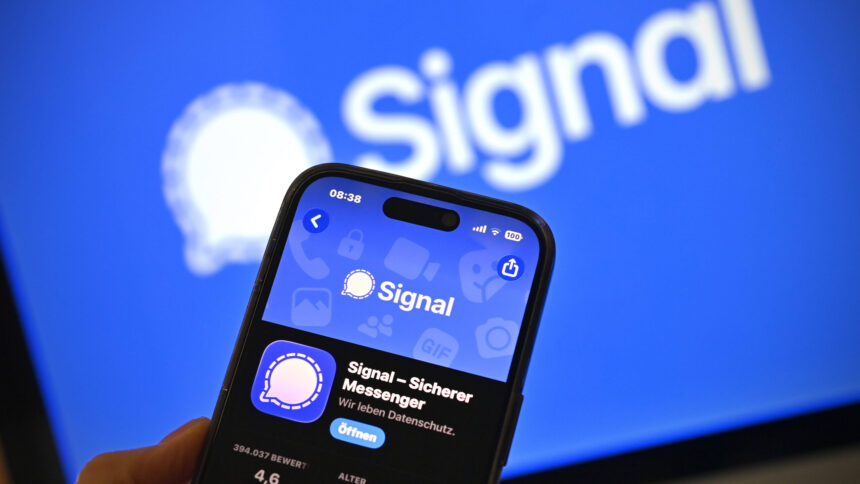 Smartphone mit geöffneter Signal-Messenger-App vor einem unscharfen Bildschirm mit dem Signal-Logo