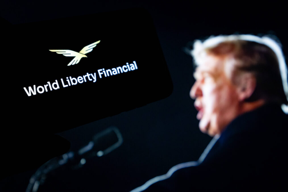 Trump am Mikro vor dem Schriftzug seines Unternehmens World Liberty Financial.