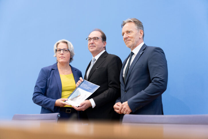 Drei Personen halten ein Papier in die Kamera