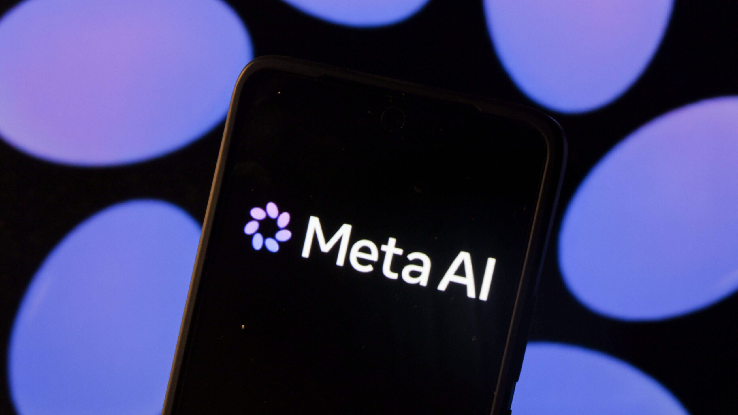 Smartphone mit dem Schriftzug 'Meta AI' vor unscharfen lila Kreisen im Hintergrund