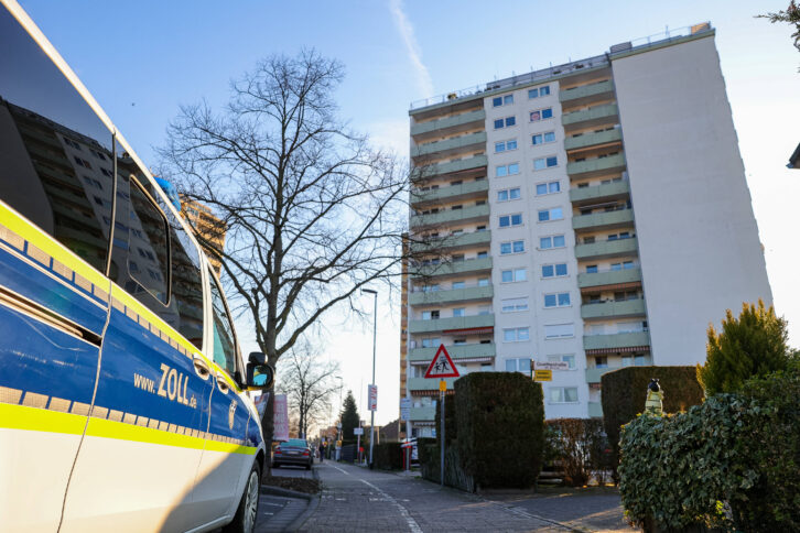 Bild eines Hochhauses, links parkt ein Fahrzeug des Zolls.
