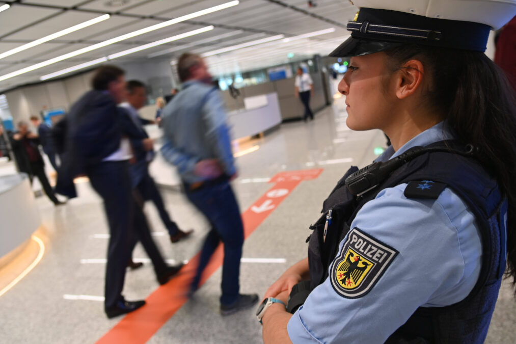 Polizistin steht hinter der Handgepaeckkontrolle,
