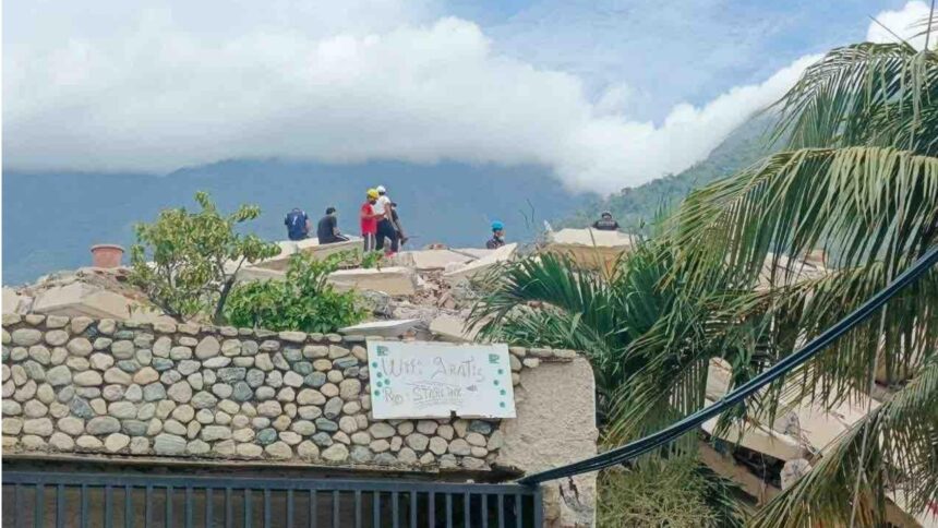 Ein leicht unscharfes Foto in einem bergigen Dorf, im Vordergrund ein Schild mit der Aufschrift "Free Wifi", im Hintergrund Katastrophenhelfer:innen