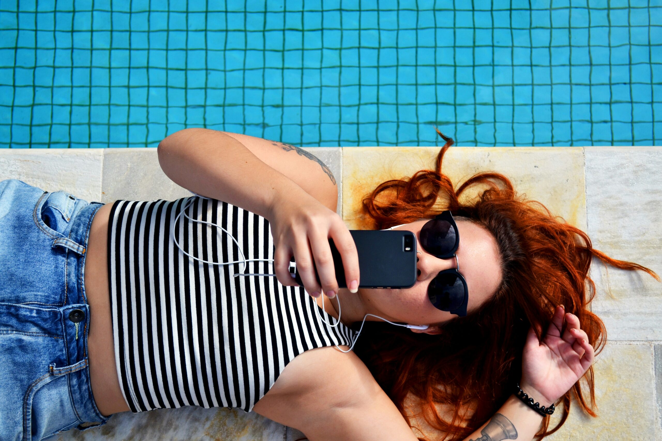 Person liegt mit Smartphone in der Hand an einem Pool.